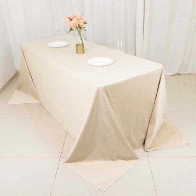 Beige tablecloth draped over a dining table with plates and a flower vase.