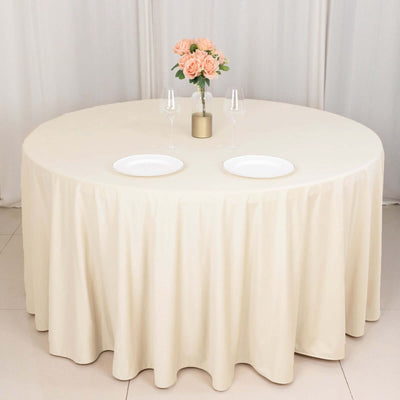 Round beige tablecloth draped over a round table with flowers and plates.