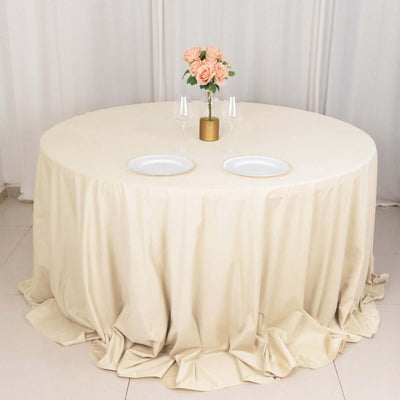 Round table set with beige tablecloth, floral centerpiece, and gold-accented plates.