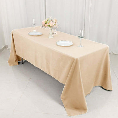 Elegant beige tablecloth set for dining with plates and flower vase.