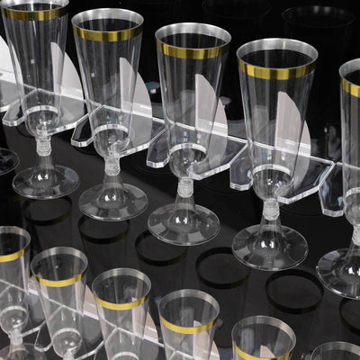 Clear plastic champagne flutes with gold rims displayed in a modern holder.