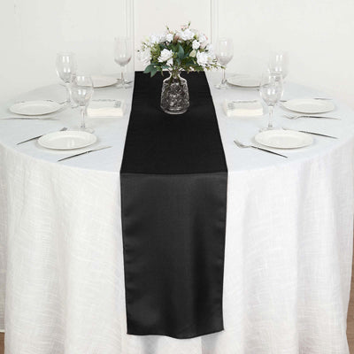 Black satin table runner on a white table with glassware and flowers.