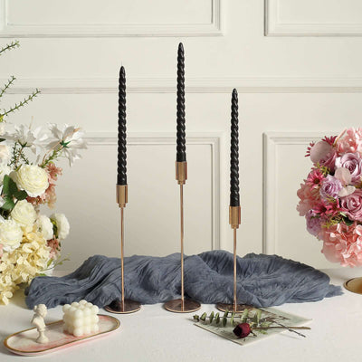 Elegant black twisted candles in gold holders on a stylish table setting.