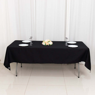 Black tablecloth draped over a table set for an event with plates and floral centerpiece.