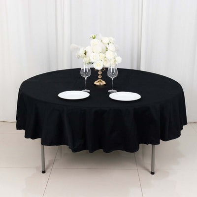 Elegant round table set with black tablecloth, white plates, and floral centerpiece.