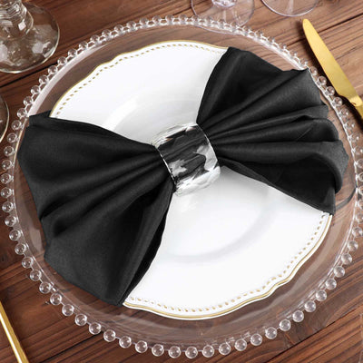 Black satin napkin bow with silver ring on a decorative plate.