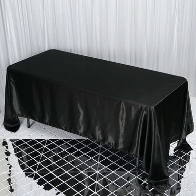 Black satin tablecloth draped over a rectangular table on a reflective surface.
