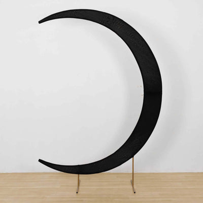 Black crescent moon sculpture on a stand against a plain background