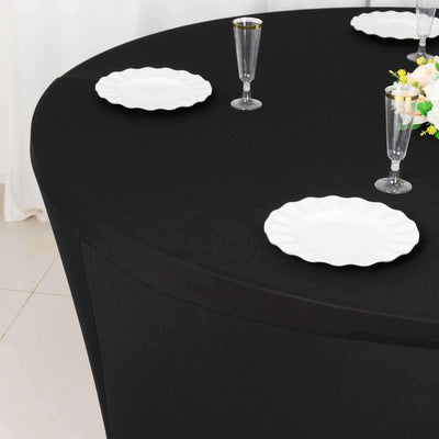 Black fitted tablecloth on a round table set with white plates and glassware.