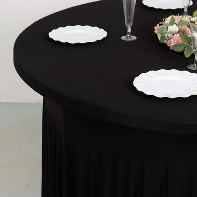 Black tablecloth draped over a round table with white plates and floral centerpiece.