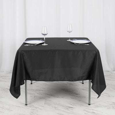 Black tablecloth draped over a table set with plates and wine glasses.