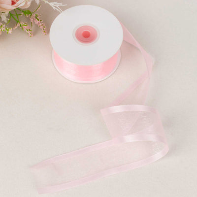 Pink sheer ribbon spool with loose ribbon on a soft surface.