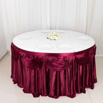 Round table with burgundy satin tablecloth and white plates, elegantly set for dining.