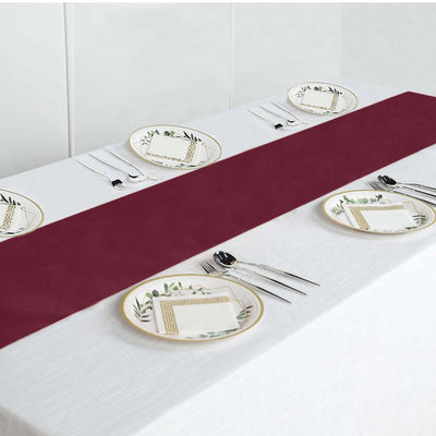 Burgundy table runner on a white table with decorative plates and cutlery.