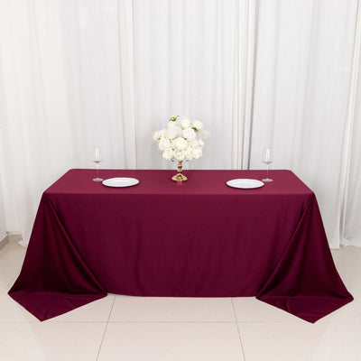 Burgundy tablecloth with white plates and floral centerpiece on a table.