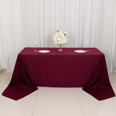 Burgundy tablecloth with white plates and floral centerpiece on a table