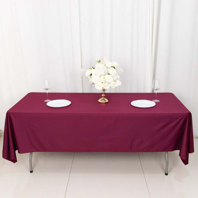 Burgundy tablecloth with plates and floral centerpiece on a dining table.