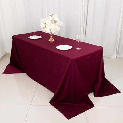 Burgundy tablecloth draped over a dining table with plates and a floral centerpiece.