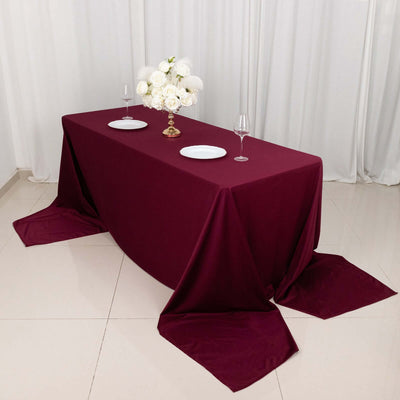 Elegant burgundy tablecloth set with white plates and floral centerpiece.