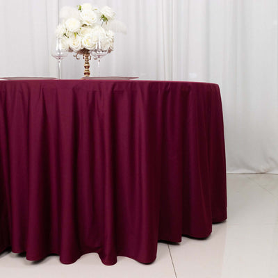 Burgundy tablecloth draping a round table with a floral centerpiece.