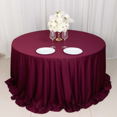 Round burgundy tablecloth draped elegantly with white roses and tableware.