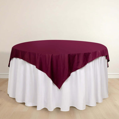 Round table with burgundy tablecloth and white skirt on a light wood floor.