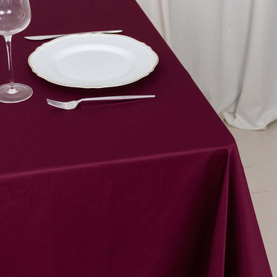 Burgundy tablecloth with white plate and cutlery set on a dining table.