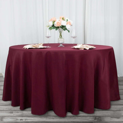 Burgundy tablecloth on a round table set with flowers and wine glasses.