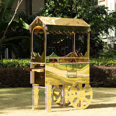 Golden decorative cart on wheels in a garden setting.