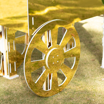 Gold wheel detail of a decorative cart on grass.