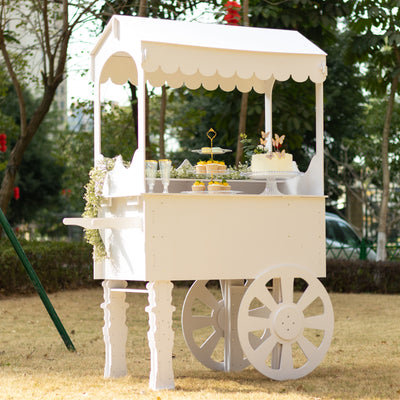 White dessert cart with wheels, decorated with flowers and pastries in an outdoor setting.