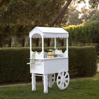White outdoor dessert cart with wheels, set in a garden backdrop.