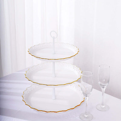 Three-tiered white serving stand with gold trim and two champagne flutes.
