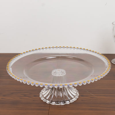 Clear cake stand with decorative beaded edge on wooden surface.