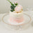Three-tiered wedding cake decorated with roses and pearls on a glass pedestal.