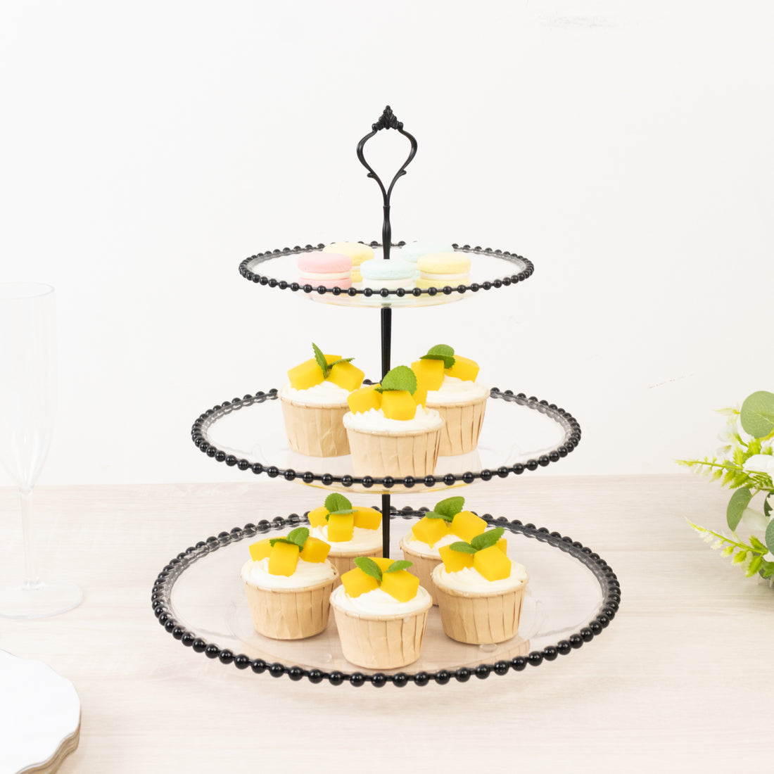 Three-tiered black cupcake stand with cupcakes and fruit decorations.