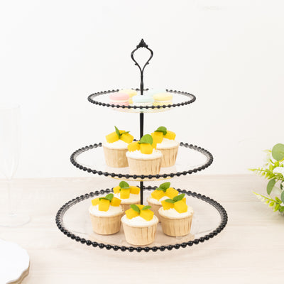 Three-tiered black cupcake stand with cupcakes and fruit decorations.