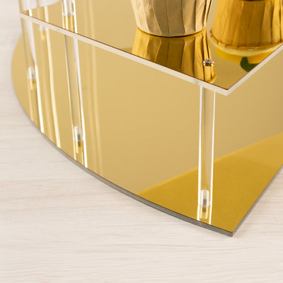Gold mirrored display shelf with transparent supports and rounded edges.