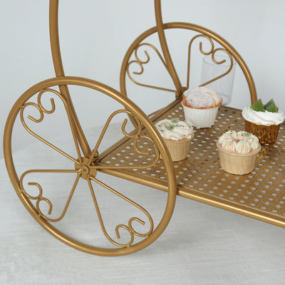 Gold dessert cart with decorative wheels and assorted cupcakes on a white background.