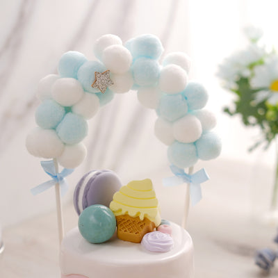 Colorful dessert-themed cake topper with pom poms and decorative elements.