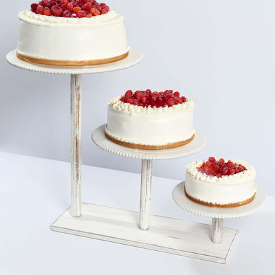 Three elegant cakes with red fruit toppings displayed on a rustic stand.
