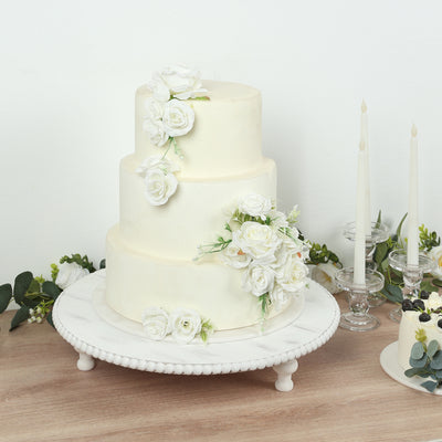 Elegant three-tier wedding cake adorned with white roses on a decorative stand.