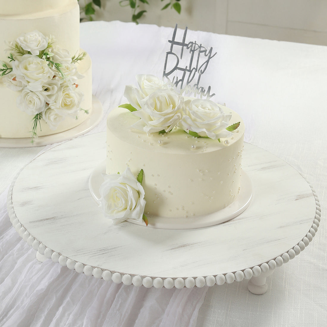 Birthday cake decorated with white roses on a cake stand.