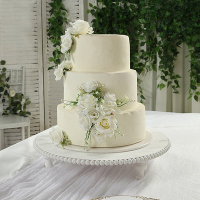Elegant three-tier wedding cake adorned with white roses and greenery.