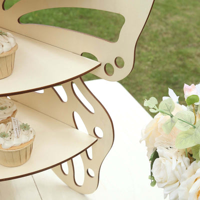Butterfly-shaped cupcake stand with cupcakes and floral arrangement in outdoor setting.