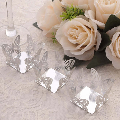 Silver butterfly-shaped cupcake holders with floral arrangement backdrop.