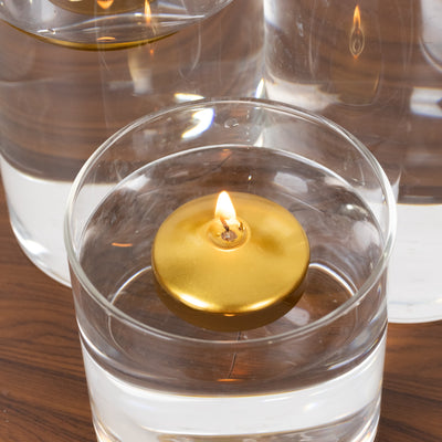 Gold floating candle in glass container filled with water.