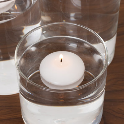 Floating white candle in clear glass vase filled with water.