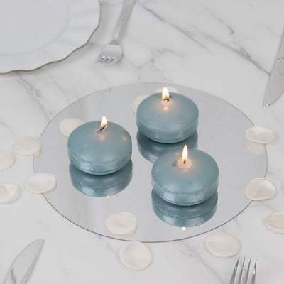Three blue round candles on a mirrored surface with rose petals around them.