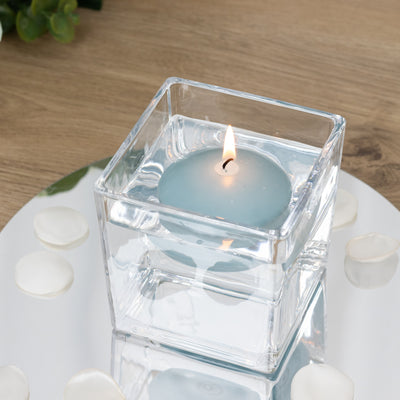 Blue floating candle in a clear glass holder on a mirrored surface.